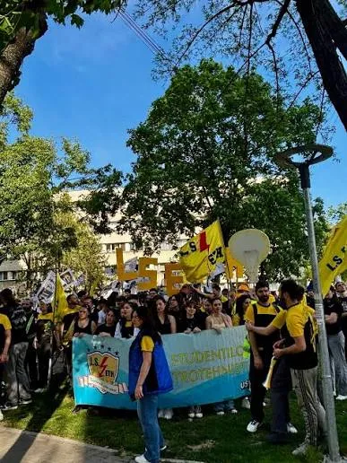 Grup numeros de studenți în zona campusului Tudor Vladimirescu, cu steaguri și bannere, într-o zi aglomerată