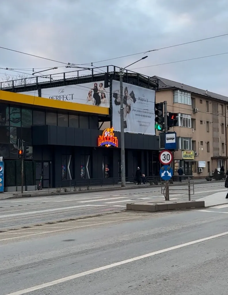 Fațada clădirii cu semnul MaxBet luminat, văzută de pe bulevardul Tudor Vladimirescu, cu trecere de pietoni și stație de transport în față